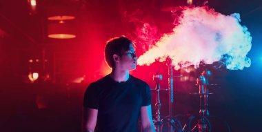 Adam nargile içiyor ve dumandan bir bulut salıyor.