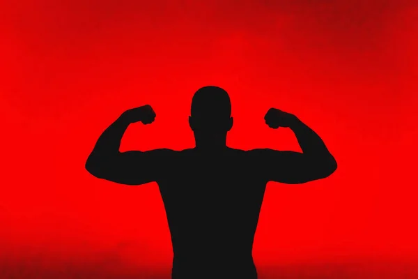 Силуэт сильного мужчины, демонстрирующего свои мускулы — стоковое фото