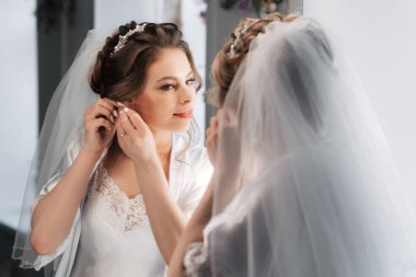 Gelin, aynada kendine bakarken kulaklarına küpe takar.