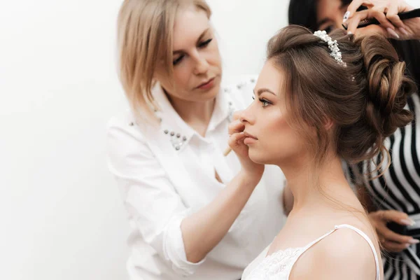 Reggeli előkészületek a menyasszonyok esküvőjére egy szépségszalonban. Egy sminkes sminkeli magát, és egy fodrász csinálja a haját. — Stock Fotó