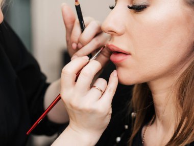 Makyöz, kuaförde çalışan bir kadın için dudak fırçasıyla dudak boyuyor.