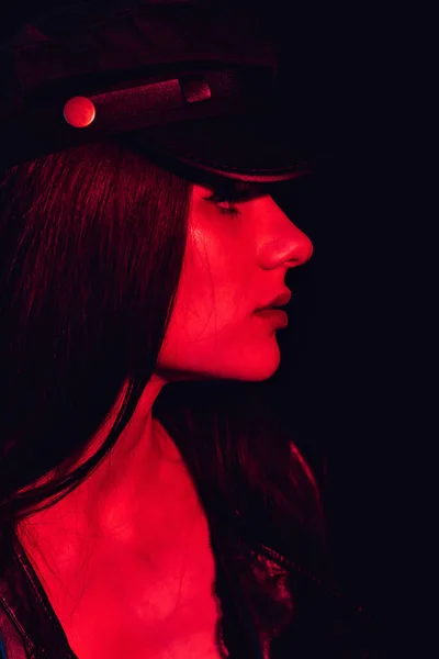 Retrato de moda de una chica de perfil en una gorra de cuero y chaqueta con una luz de neón roja — Foto de Stock