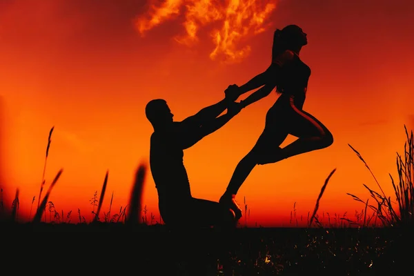 Silhouet van een koppel dat een yoga-oefening doet bij zonsondergang in de zomer — Stockfoto