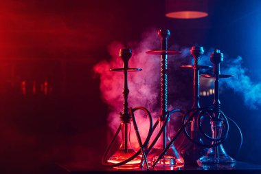 Kavanozlarda shisha kömürleri olan nargileler, neon ışıklı dumanların arka planına karşı.