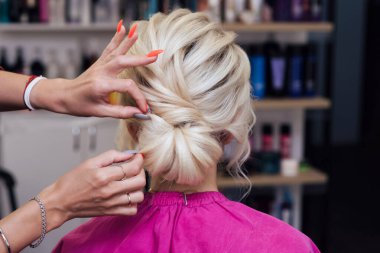 hairdresser makes his own hands hairstyle a bun on the head of a blonde girl clipart
