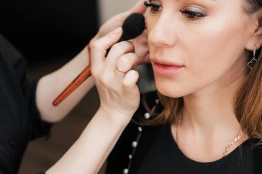 Güzellik salonundaki bir kadının yüzüne makyaj yapmak makyaj sanatçısı eli fırçayla yapar.