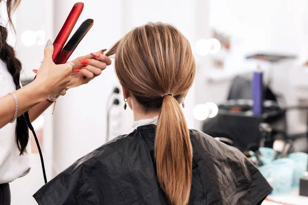 Kadeřnice dělá účes pro ženu se světle hnědými dlouhými vlasy — Stock fotografie