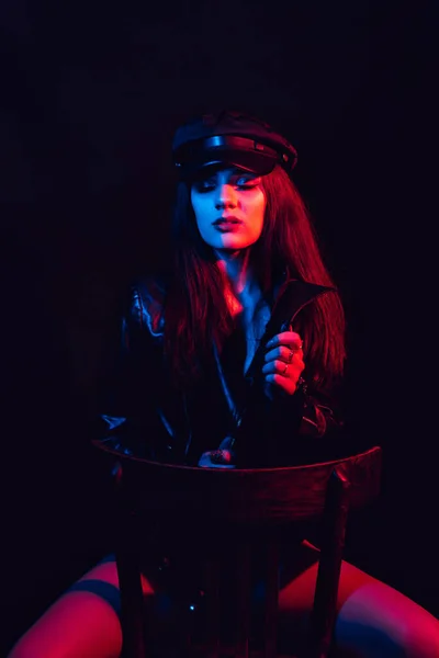 Retrato de moda de una chica con estilo en una chaqueta de cuero y gorra con una luz de neón —  Fotos de Stock