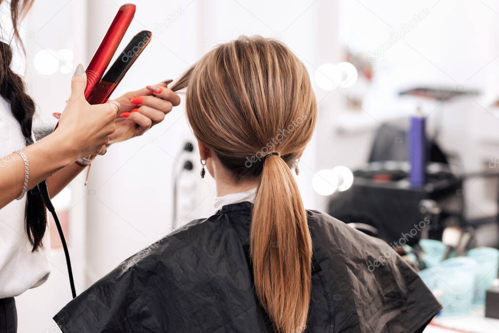 hairstylist makes a hairstyle for a woman with light brown long hair