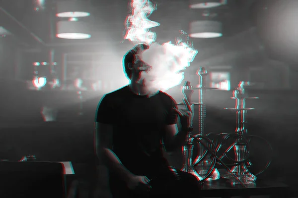 young man smokes a hookah and lets out a cloud of smoke