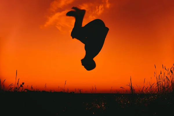 Der Mensch führt ein Element von Parkour aus. Silhouette macht einen Salto bei Sonnenuntergang im Freien — Stockfoto