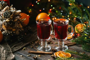 Noel ağaçlarıyla süslenmiş ahşap bir masada sıcak şaraplı bardaklar. Geleneksel portakal dilimli alkollü kış içeceği.