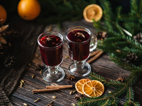Δύο ποτήρια με ζεστό κρασί με φέτες πορτοκαλιού και κανέλα, κάρδαμο σε ξύλινο τραπέζι — Φωτογραφία Αρχείου
