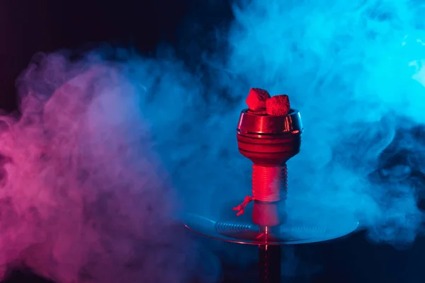 Carvões shisha quentes vermelhos em uma tigela de metal hookah contra um fundo de fumaça multicolorida — Fotografia de Stock