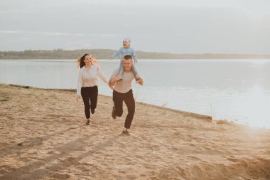 Oğulları sahilde oynarken ve eğlenirken mutlu genç bir aile.