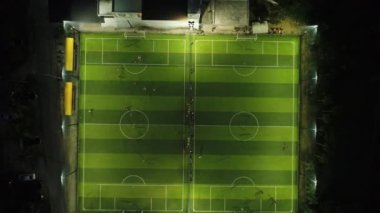 Hava. Fotoğraf makinesi üst aşağı hareket. Üstten görünüm iki futbol sahası gece zaman. Futbol oynayan takımlar.