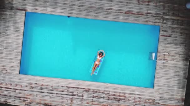 AERIAL. Top view. Camera zooming. Outdoor lifestyle portrait of young pretty sexy girl posing with neon bright swimming mattress at the pool in luxury villa at the jungle, wearing bikini and — Stock Video