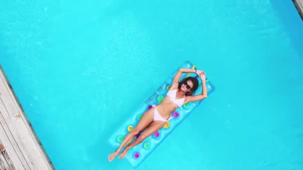 AERIAL. Top view. Camera zooming. Outdoor lifestyle portrait of young pretty sexy girl posing with neon bright swimming mattress at the pool in luxury villa at the jungle, wearing bikini and — Stock Video