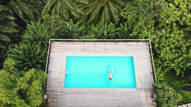 AEREALE. Vista dall'alto. Stile di vita all'aperto ritratto di giovane ragazza piuttosto sexy in posa con neon luminoso materasso nuoto in piscina in villa di lusso nella giungla, indossando bikini e occhiali da sole, rilassarsi — Video Stock