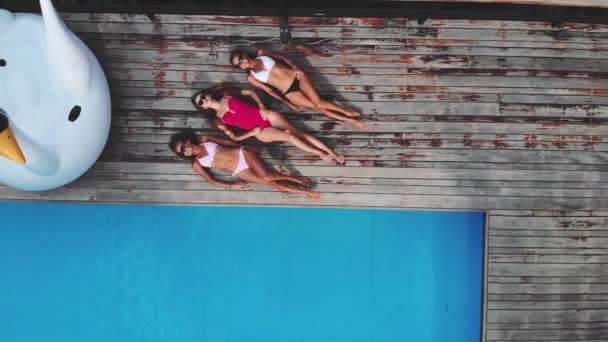 AERIAL. Top view of three young woman in sun glasses, lying near pool at luxury jungle villa. Three friends relaxing at the swimming pool. — Stock Video