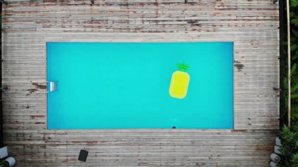 AERIAL. floating pineapple, beach mattress in water pool top view of crystal clean water surface, sun shine bright water-pool looping slow motion background — Stock Video