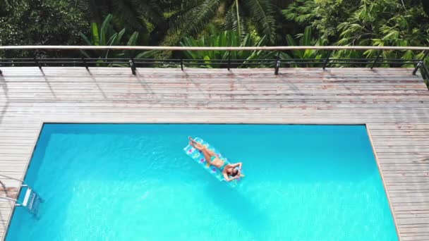 Retrato de estilo de vida al aire libre de la joven chica bastante sexy nadando con colchón de natación brillante de neón en la piscina, usando bikini y gafas de sol, vista de la selva, relajarse y divertirse en vacaciones . — Vídeos de Stock