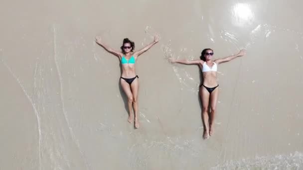 トップがビキニを着て横になっているとタイ、ドローンから空撮のターコイズ ブルーの海の水と白い砂浜でリラックスの 2 つの若い女性を見る — ストック動画