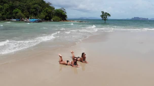 Top view two young woman in a bikini lying and relaxing on the white sandy beach with turquoise sea water of thThailand, aerial view from drone — стоковое видео