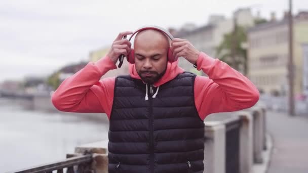 Młody człowiek włączyć muzykę na telefon i uruchomiona na most nad rzeką w mieście — Wideo stockowe