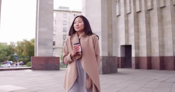 Ung asiatisk kvinna med kaffe i en pappersmugg i en stadsgata. Flicka med kaffe att gå — Stockvideo