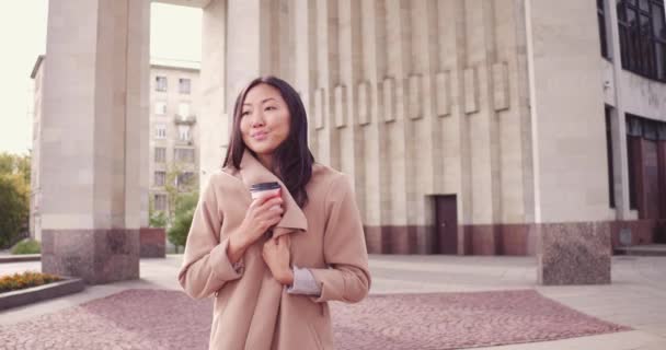 Jonge Aziatische vrouw met koffie in een papier beker in een stad straat. Meisje met koffie te gaan — Stockvideo