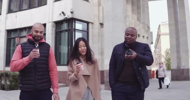 Trois jeunes gens multiethniques discutent et mangent pour aller manger tout en se tenant debout en plein air dans la journée ensoleillée d'automne. Se faire des amis, se réunir concept de réunion . — Video