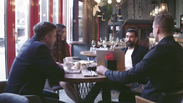 Группа молодых бизнесменов собралась вместе, чтобы обсудить творческую идею в кафе. Используя современные гаджеты, мы можем повысить производительность труда. . — стоковое видео
