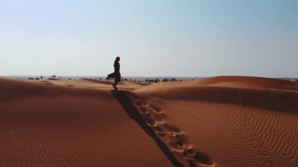 Antenn. Visa från en drönare som flyger bredvid en kvinna i abaya Förenade Arab Emirateswalking på dynerna i öknen i kvarteret tom. Abu Dhabi, Förenade Arabemiraten. — Stockvideo