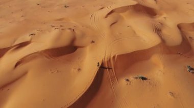 AERİAL. Dubai çölünde gün batımında kumulda yürüyen uzun elbiseli bir kadın.