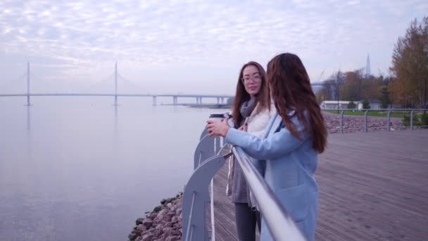 Outdoor Mode Porträt von zwei fröhlichen Mädchen, asiatische und arabische Kaffee trinken. Stehen und reden auf der Böschung. — Stockvideo