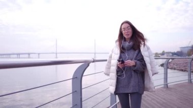 Akıllı telefon ayakta set of deniz kıyısında kullanan Genç Asyalı kadın. Gri kazak ve beyaz ceket holding arka plan açık su, mobil aygıtta giymiş erkek yakın çekim.