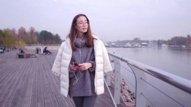 Akıllı telefon ayakta set of deniz kıyısında kullanan Genç Asyalı kadın. Gri kazak ve beyaz ceket holding arka plan açık su, mobil aygıtta giymiş erkek yakın çekim.