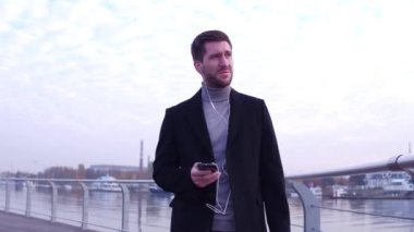 Ciddi adam zaman el altında kontrol saatleri, şehir setin güzel arka plan manzaralı yürüyüş.