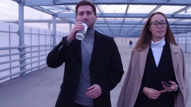 Zakenman en zakenvrouw wandelen langs straat bedrijf afhaalmaaltijden koffie — Stockvideo