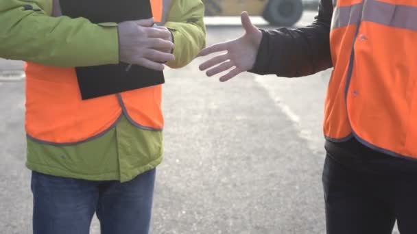 Deux ingénieurs portant des vêtements de travail orange se réunissant pour serrer la main sur un grand inventaire de suivi commercial, gros plan . — Video