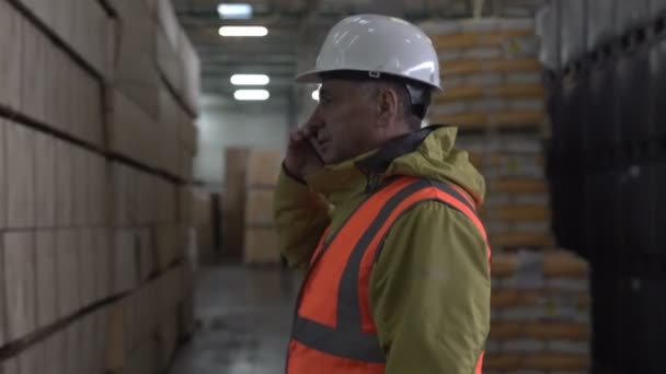 Trabajador de almacén en casco usando teléfono móvil — Vídeos de Stock