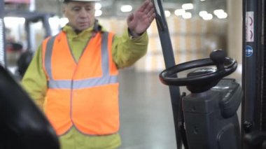 Yetişkin forklift sürücüsü içinde geliyor, tablet kontrol ve notlar makine içinde beyaz işçisi ve turuncu workwear yoğunlaştı.
