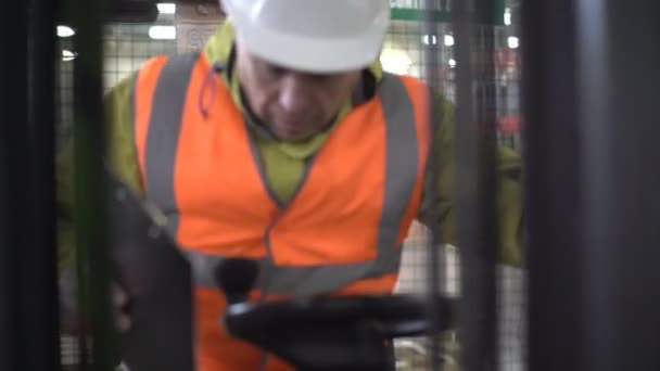 Concentrated adult forklift driver comes inside, checking the tablet inside machine. — Stock Video