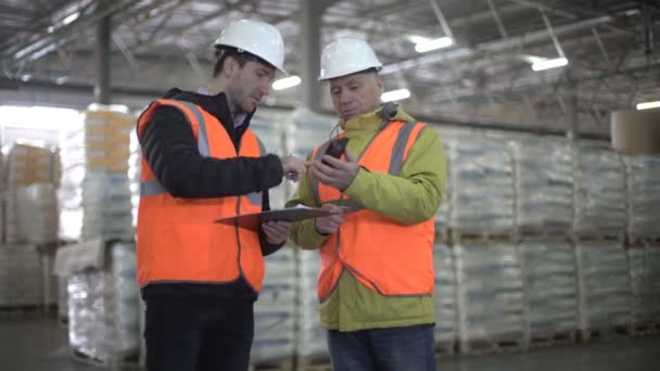 Dos hombres de negocios discutiendo el nuevo proyecto, usando el teléfono celular en el almacén . — Vídeos de Stock