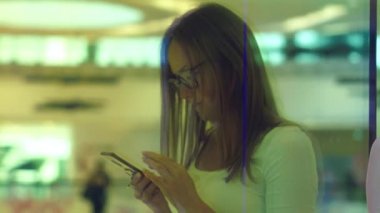 Pencerenin aynaya odaklan. Yazarak bir alışveriş merkezinde akıllı telefon, arka plan üzerinde renkli windows üzerinde kadın