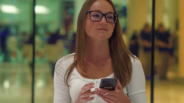 Vrouw te typen op de slimme telefoon in een winkelcentrum centrum, kleurrijke windows op achtergrond — Stockvideo