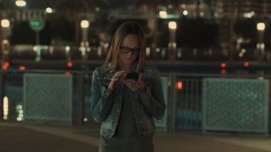 Güzel genç şık kadın modern smartpone, onun cep telefonundan kısa mesaj yazarak hipster kadın blogger kullanarak gece şehrin sokaklarında yürüyüş