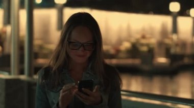 Güzel genç şık kadın modern smartpone, onun cep telefonundan kısa mesaj yazarak hipster kadın blogger kullanarak gece şehrin sokaklarında yürüyüş