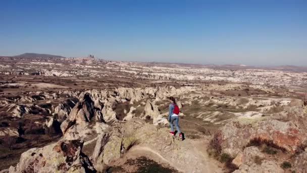 AERIAL. Cámara moviéndose alrededor de mujer joven levantando las manos en la montaña por la mañana. Viajero con mochila roja de pie en la montaña por la mañana . — Vídeos de Stock